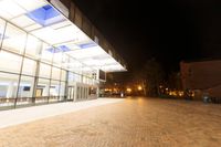 a large glass building on a bricked floor in front of a parking lot at night