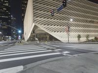 a modern building at night with traffic lights on the ground and street signs in front