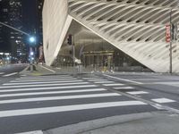 a modern building at night with traffic lights on the ground and street signs in front