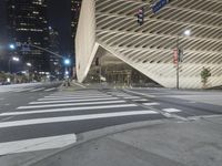 a modern building at night with traffic lights on the ground and street signs in front