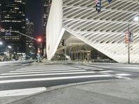 a modern building at night with traffic lights on the ground and street signs in front