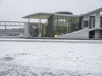 a large glass and stone building next to a river with snow on the ground and a person walking across the bridge