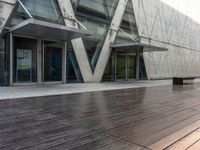 an empty wooden walkway outside a modern building with glass doors and railings on it