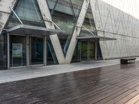 an empty wooden walkway outside a modern building with glass doors and railings on it