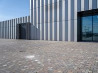 the front door and side wall of a modern building on an urban street and brick road