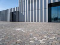 the front door and side wall of a modern building on an urban street and brick road