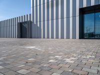 the front door and side wall of a modern building on an urban street and brick road