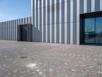 the front door and side wall of a modern building on an urban street and brick road