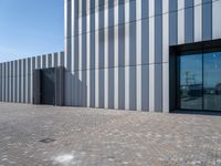 the front door and side wall of a modern building on an urban street and brick road