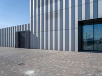 the front door and side wall of a modern building on an urban street and brick road