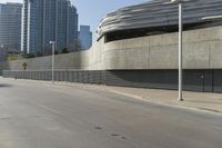 an empty street with modern buildings in the background and tall concrete blocks surrounding it, on a sunny day