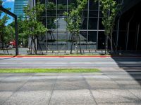 the bus stop sign is near a building with large windows and tree lined sidewalk in front of it