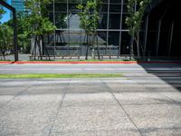 the bus stop sign is near a building with large windows and tree lined sidewalk in front of it