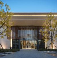 the entrance to a modern business building at night with tall trees in the foreground