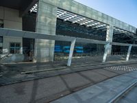 a bench sitting in front of a glass building on top of stone pavements below a metal ceiling