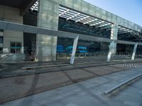 a bench sitting in front of a glass building on top of stone pavements below a metal ceiling