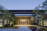 large glass walled entry with glassy fountain in front of entrance and glass wall reflecting water feature at dusk