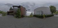 a fish eye lens shot of a large circular building next to a parking lot with trees on one side and a fence in front