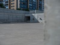 the empty parking lot in front of a wall with apartment buildings on it and a skateboarder on a ramp