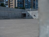 the empty parking lot in front of a wall with apartment buildings on it and a skateboarder on a ramp