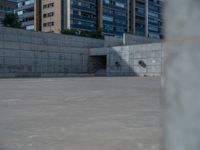 the empty parking lot in front of a wall with apartment buildings on it and a skateboarder on a ramp