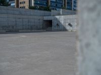 the empty parking lot in front of a wall with apartment buildings on it and a skateboarder on a ramp