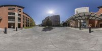 360 - view looking down a paved street past buildings and trees in the background with a small sun shining over them