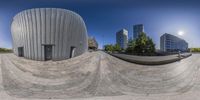 fisheye panoramic view of a modern city with a man skateboarding next to a giant round sculpture