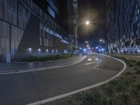 a empty road in the middle of a city at night with street lamps on both sides and building lights on all three sides of it