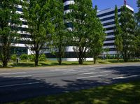 an empty street in front of a building that is surrounded by trees and grass in front of the building