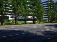 an empty street in front of a building that is surrounded by trees and grass in front of the building