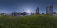 a panorama of some buildings in the distance with a river running under it on the grass