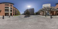 360 - view looking down a paved street past buildings and trees in the background with a small sun shining over them