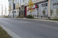 an empty street in a modern city with shops and trees on either side of it