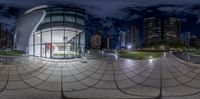 the photo has a view of a modern city at night from the bottom of the glass facade