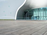 the building has glass and steel panels in front of it and people walking beside it