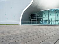 the building has glass and steel panels in front of it and people walking beside it