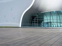 the building has glass and steel panels in front of it and people walking beside it