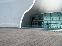 the building has glass and steel panels in front of it and people walking beside it