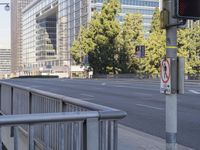 a metal fence next to a street with tall buildings in the background and no stopping sign on the sidewalk