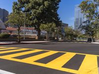 two trees standing next to a street with yellow painted markings on it and two vehicles passing through