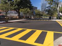 two trees standing next to a street with yellow painted markings on it and two vehicles passing through