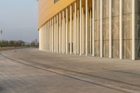 two people are walking down an empty road by tall buildings that have columns in front of them