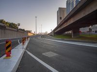 a city street is under an overpass near tall buildings and some grass and trees