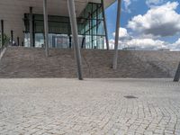 a person on a bike walking through a stone building entrance, in front of an enormous glass wall and stairs