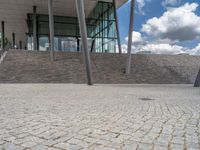 a person on a bike walking through a stone building entrance, in front of an enormous glass wall and stairs