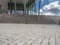 a person on a bike walking through a stone building entrance, in front of an enormous glass wall and stairs