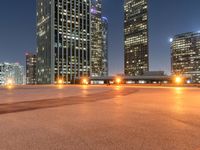 view of an empty parking lot with tall skyscrapers at night from the top of a road