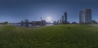 a panorama of some buildings in the distance with a river running under it on the grass