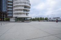 a empty parking lot next to tall buildings with cars in front of it and trees in the background